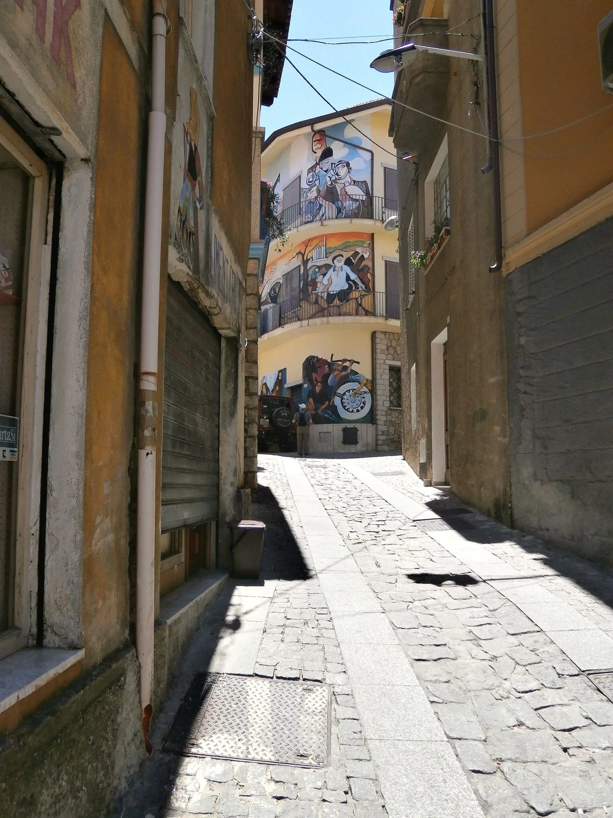 Vicolo lastricato di Orgosolo che sale verso una casa dipinta con grandi murales colorati