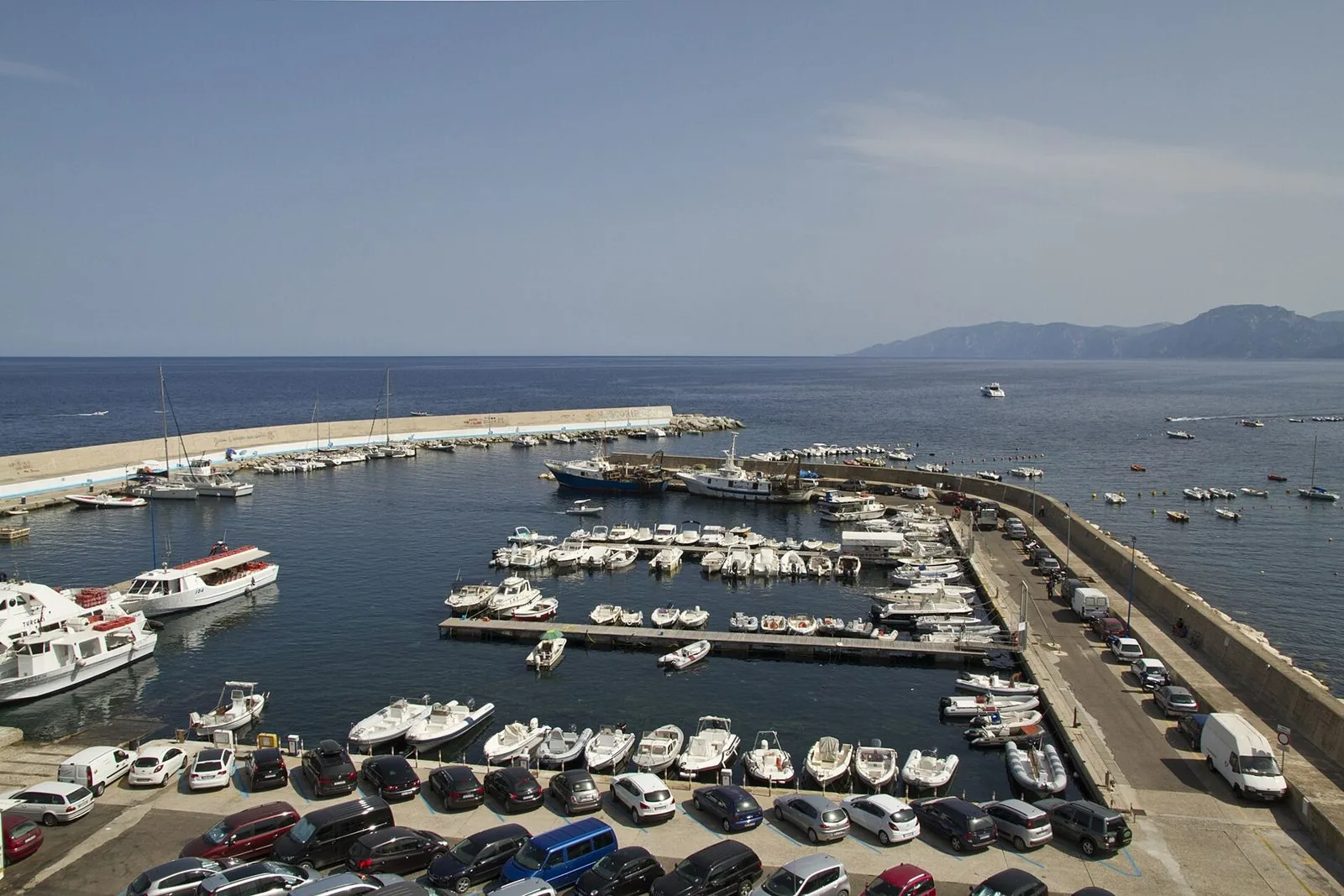 Veduta dall'alto del porto di Cala Gonone con barche ormeggiate, il molo e la costa montuosa sullo sfondo