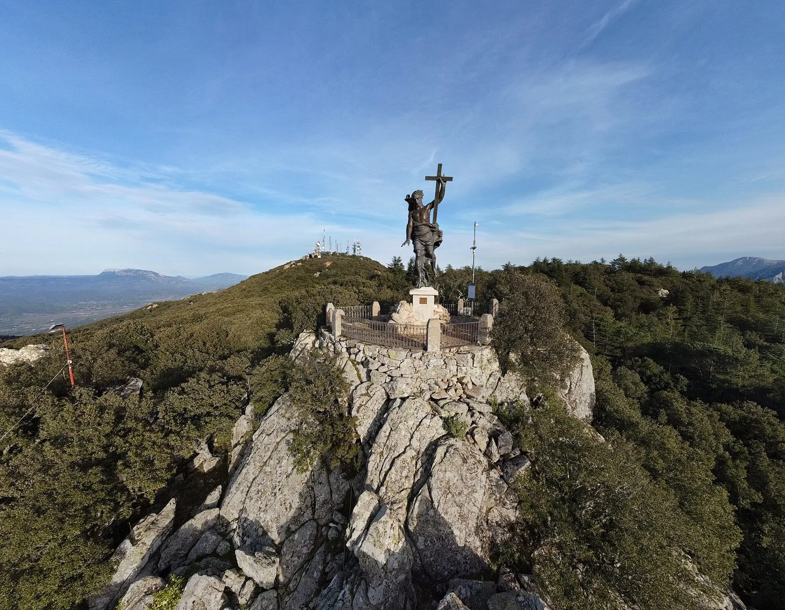 Statua bronzea del Redentore sulla cima rocciosa del Monte Ortobene, circondata dal bosco, con le montagne della Barbagia sullo sfondo